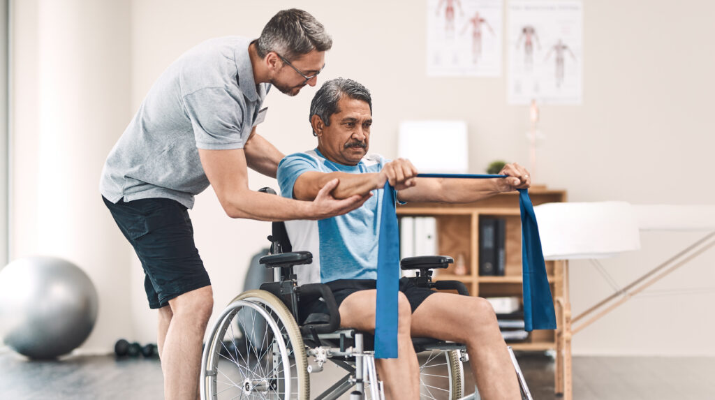 A man assisting a person with disability to stand up from a wheelchair.