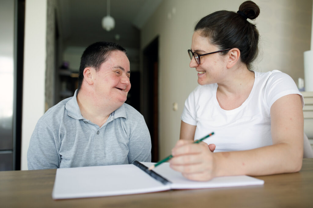 A person with disability smiling at a nurse as she writes notes on paper.